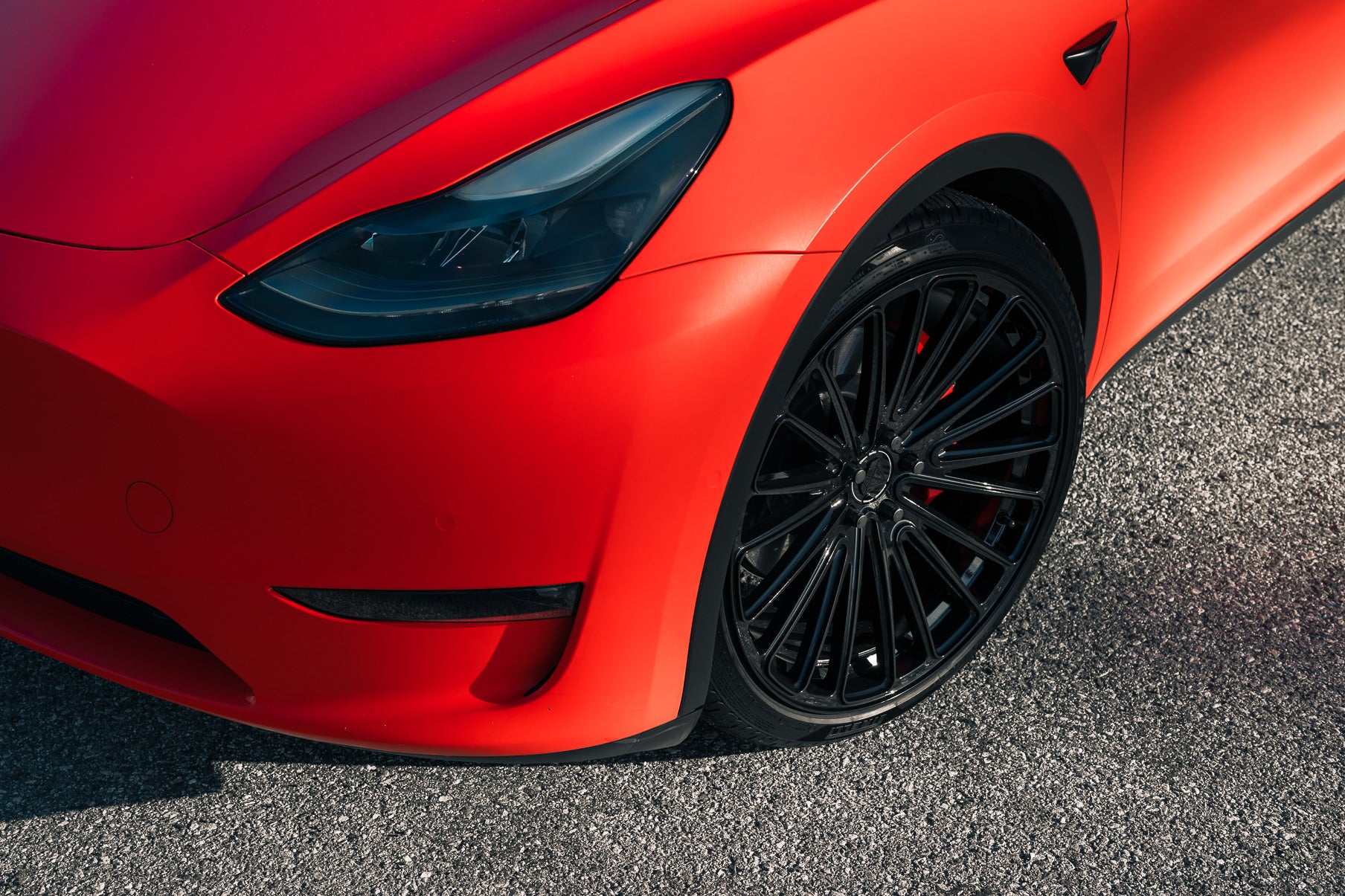 Close-up of a red car's front wheel with black rims on a pavement.
